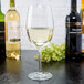A clear 18 oz. wine glass filled with white wine, surrounded by bottles of wine on a dark surface.