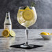 A large gin and tonic glass filled with a clear beverage, ice, lemon and lime slices, and a sprig of rosemary, placed on a black napkin on a marble surface.