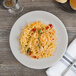 A white porcelain coupe plate with a serving of shrimp pasta, garnished with herbs.