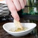A small, bright white oval porcelain bowl containing oil and herbs, with a piece of bread being dipped into it.