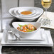 A small bright white oval porcelain bowl placed on a stack of white plates.