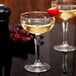 A clear Libbey Speakeasy 8.5 oz. coupe glass filled with a light-colored beverage and garnished with a strawberry on the rim.