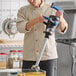 A heavy-duty electric immersion blender with a long stainless steel shaft being used in a commercial kitchen.