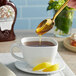 A person pouring Dutch Gold Buckwheat Honey from a spoon into a cup of tea.