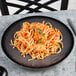 A black porcelain coupe plate holding a serving of pasta with shrimp and tomato sauce.