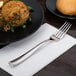 A stainless steel dinner fork with a textured handle placed on a white napkin.