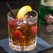 A clear, faceted 12.5 oz. rocks glass filled with an old fashioned cocktail, garnished with cherries and an orange peel.
