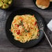 A black matte porcelain coupe plate holding a serving of pasta with shrimp and vegetables.
