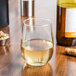 A clear, stemless white wine glass filled with white wine, placed on a wooden surface.
