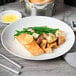A white porcelain coupe plate with a serving of salmon, roasted potatoes, and green beans.