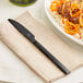 A black stainless steel dinner knife placed on a beige napkin.