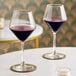 A pair of clear wine glasses partially filled with red wine, placed on a white table.