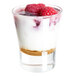 A small clear glass filled with layered dessert, including a crumb base, creamy filling, and raspberries on top.