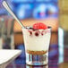 A small clear glass filled with layered dessert, topped with raspberries and a spoon, identified as a Libbey Series V 2.25 oz. shot or espresso glass.
