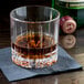 A clear Spiegelau Perfect Serve 9.25 oz. rocks glass containing a dark beverage, placed on a black napkin.