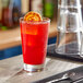 A clear 14 oz. stackable mixing glass filled with a red beverage and garnished with a dried citrus slice.