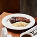 A white porcelain plate with a serving of grilled steak and a portion of rice.