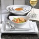 A bright white oval porcelain bowl with a 10 oz. capacity, shown as part of a table setting.