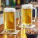 A large clear glass beer mug filled with light beer and topped with foam, placed on a coaster.