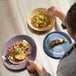 A mauve oval terracotta platter holding a plated meal, shown alongside other colorful dishes on a table.