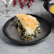 A black porcelain plate with a slice of spinach and cheese pie on it.