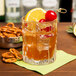 A clear, textured rocks glass filled with a cocktail, garnished with a lemon slice and cherries, placed on a green napkin.