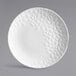 A white porcelain round coupe plate with a textured geometric pattern on part of the surface.