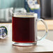 A clear glass mug filled with black coffee on a wooden surface.