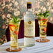 A bottle of Liber & Co Premium Tonic Syrup 750 mL placed on a table with two garnished glasses of tonic drinks.