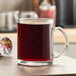 A clear glass mug filled with black coffee sits on a table next to a McCafe Premium Roast Coffee K-Cup pod.