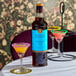 A 750 mL bottle of Liber & Co Demerara Gum Syrup displayed on a table with colorful cocktails.