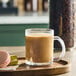 A clear glass mug filled with coffee sits on a wooden tray next to two macarons.