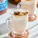 A glass mug filled with a chai tea latte topped with whipped cream, cinnamon, and a star anise.