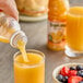 A bottle of Tropicana orange juice blend being poured into a glass, with another glass of juice and a bowl of mixed berries nearby.