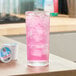 A tall glass of pink strawberry acai iced refresher with ice, next to single serve Keurig K-Cup pods.