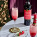 A bottle of Liber & Co Raspberry Gum Syrup alongside a raspberry cocktail and fresh raspberries on a table.