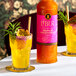 A bottle of Liber & Co Tropical Passionfruit Syrup 750 mL placed next to two glasses of a yellow tropical drink garnished with passionfruit and greenery.