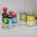 A clear plastic stackable storage tray holding canned goods and spice containers.
