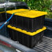 A pair of large black industrial storage totes with yellow lids secured in the bed of a pickup truck.