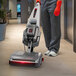 A cordless walk-behind cylindrical floor scrubber with a squeegee being used to clean a hallway floor.