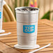 A 24 oz. aluminum cup with a blue 'Top Cup' logo, filled with ice and placed on a wooden table.