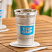 A 9 oz. aluminum cup with a blue 'Top Cup' logo, filled with ice and placed on a wooden table.