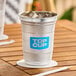 A 16 oz. aluminum cup with a blue 'Top Cup' logo, filled with ice and placed on a coaster.