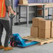 A blue Lavex manual pallet jack with 27-inch by 63-inch forks being used to move a wooden pallet loaded with cardboard boxes in a warehouse setting.