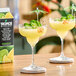 A carton of Tropics Mixology Margarita Frozen Beverage Mix next to two margarita glasses garnished with jalapeño slices and cocktail umbrellas.