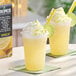 A plastic cup filled with a yellow frozen lemon beverage topped with whipped cream and garnished with a lime slice.