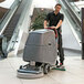 A commercial floor scrubber with a traction drive being used to clean tile flooring in a shopping mall.