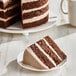 A slice of vegan chocolate layer cake with chocolate frosting, served on a white plate.