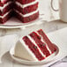 A slice of vegan red velvet naked cake with white frosting layers on a plate.