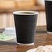 A black 12 oz. double wall ripple paper hot cup filled with coffee.